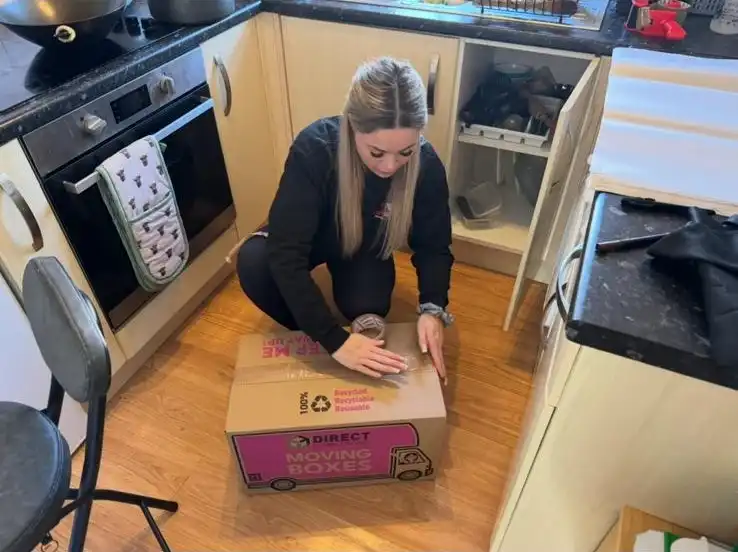 Girl packing a box sitting on the kitchen floor.